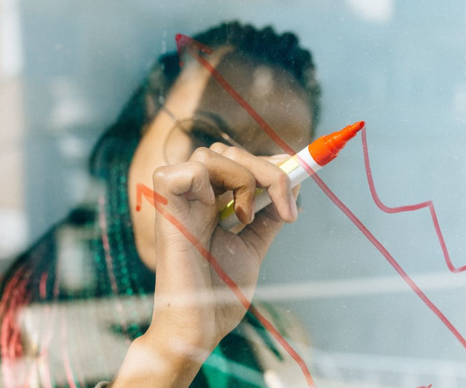 person writing on glass board with sketch marker in red